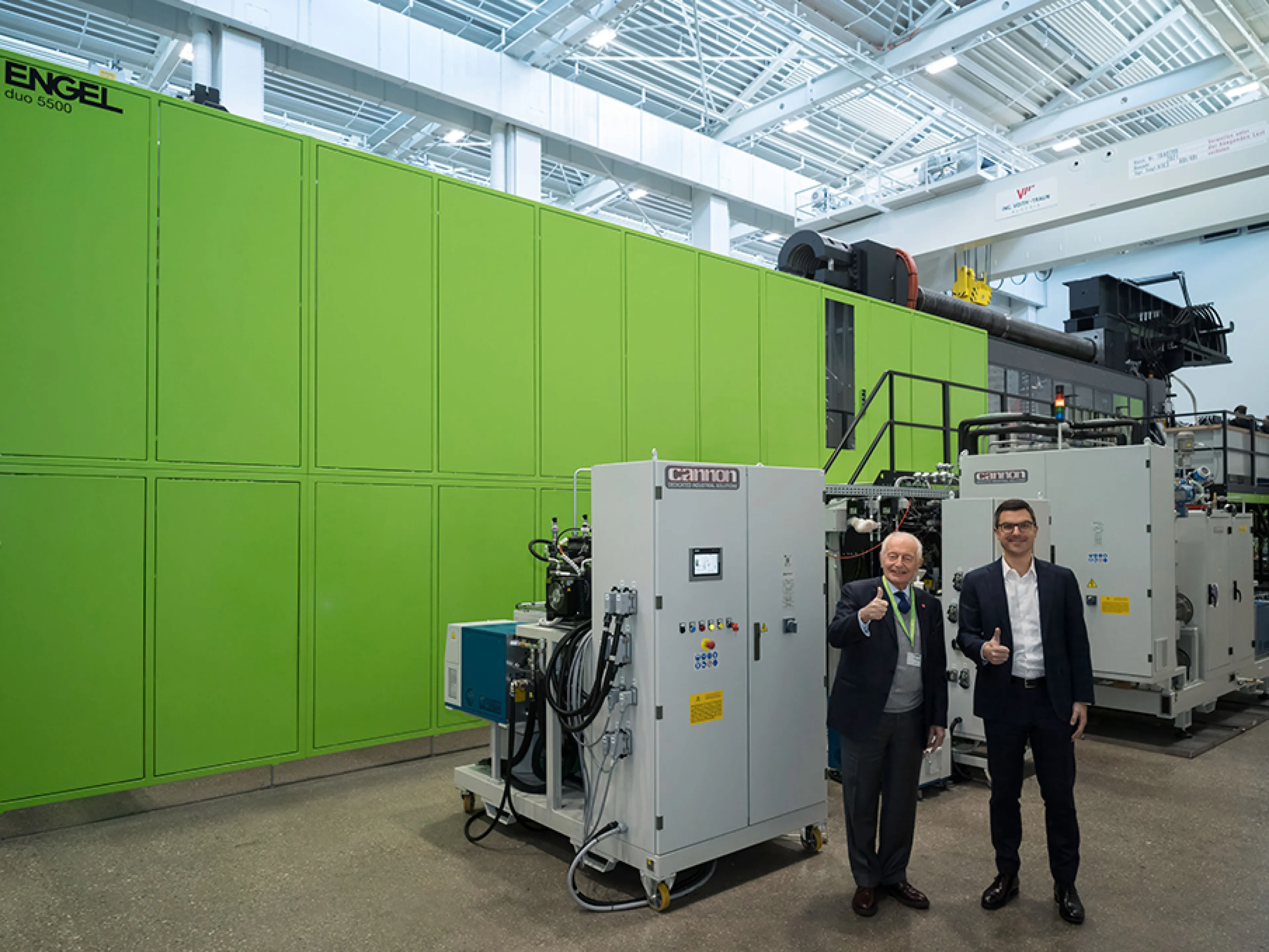 Marco Volpato (links), Präsident und Vorstandsvorsitzender der Cannon Group, und Stefan Engleder (rechts), CEO der Engel Group, vor der weltweit größten Spritzgießzelle mit PUR-Anlage in einem Technikum.